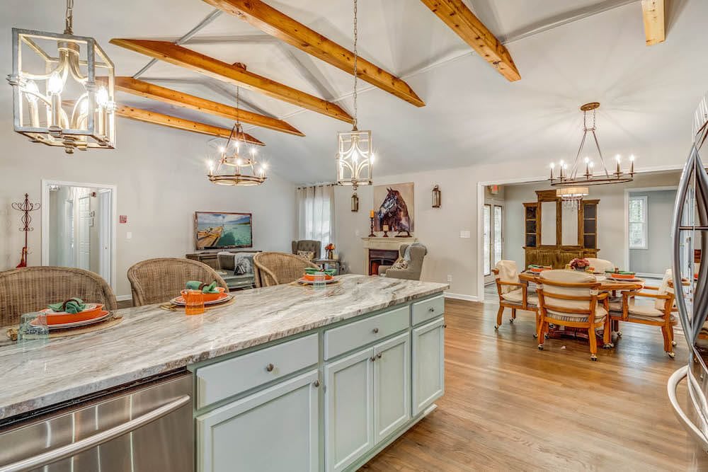 A spacious kitchen and dining area featuring wooden beams, elegant chandeliers, and a marble countertop island.