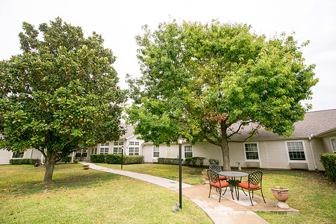 A serene outdoor area with a pathway, surrounded by trees and residential buildings.