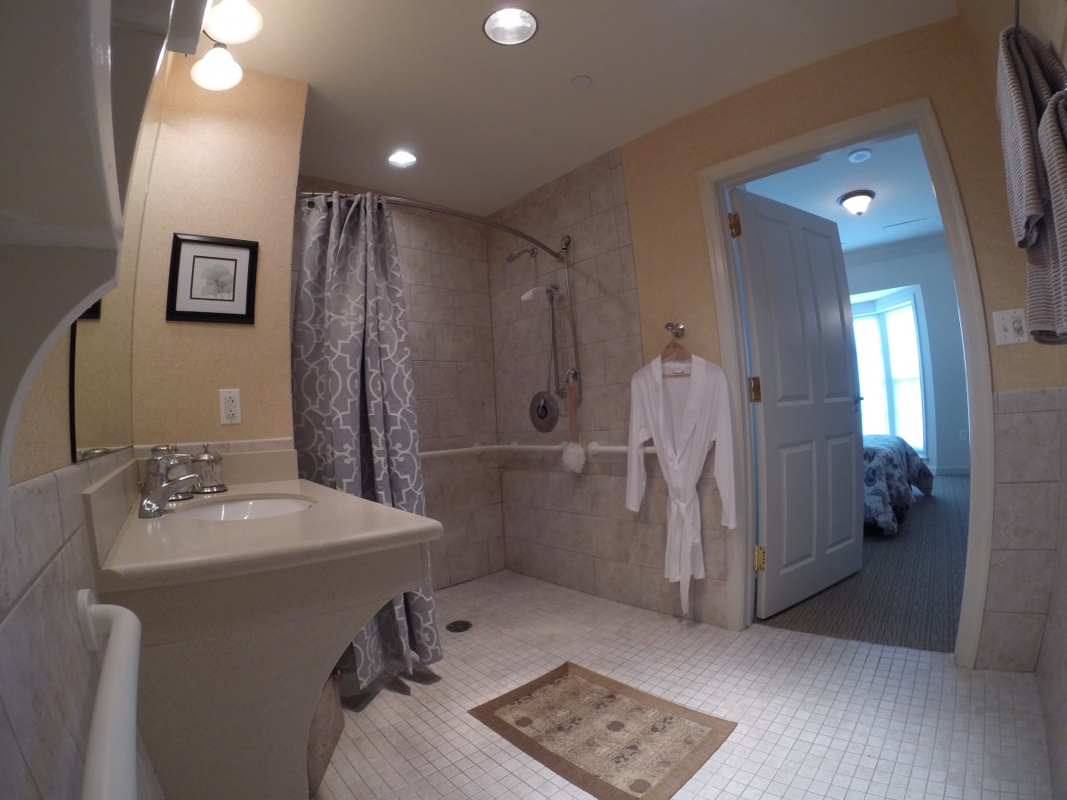 A well-lit bathroom with a shower area, robe, and sink.