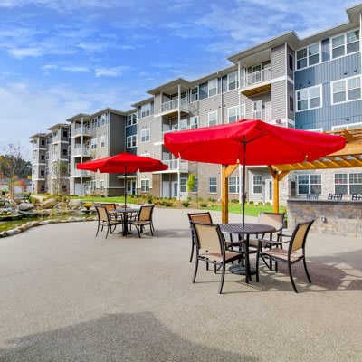 Modern apartment complex with outdoor patio seating and red umbrellas.