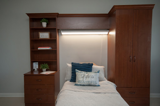A cozy modern bedroom featuring a neatly made bed, stylish pillow, and a wooden shelf with decorative plants.