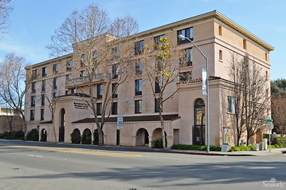 A street view of a multi-story hotel building with trees and a clear sky.