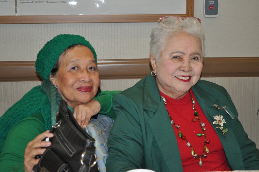 Two women sitting together, smiling and dressed in festive colors.