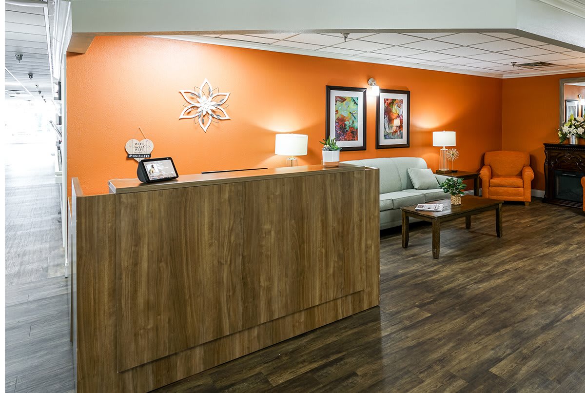 A welcoming reception area with an orange accent wall, featuring a wooden desk, comfortable sofa, and decorative artwork.