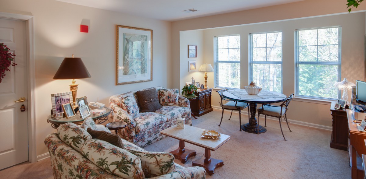 A cozy living room with floral-patterned furniture and a dining area by the window.