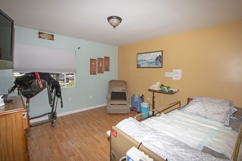 A room featuring a hospital bed and medical equipment, with artwork on the walls and a comfortable chair in the corner.