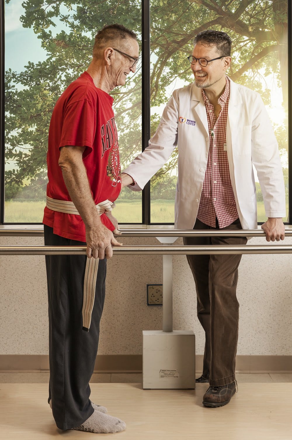 A therapist assists a patient with physical therapy exercises using parallel bars.