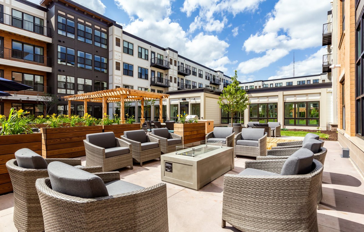 A modern outdoor patio area at an apartment complex with comfortable seating and greenery under a bright sky.