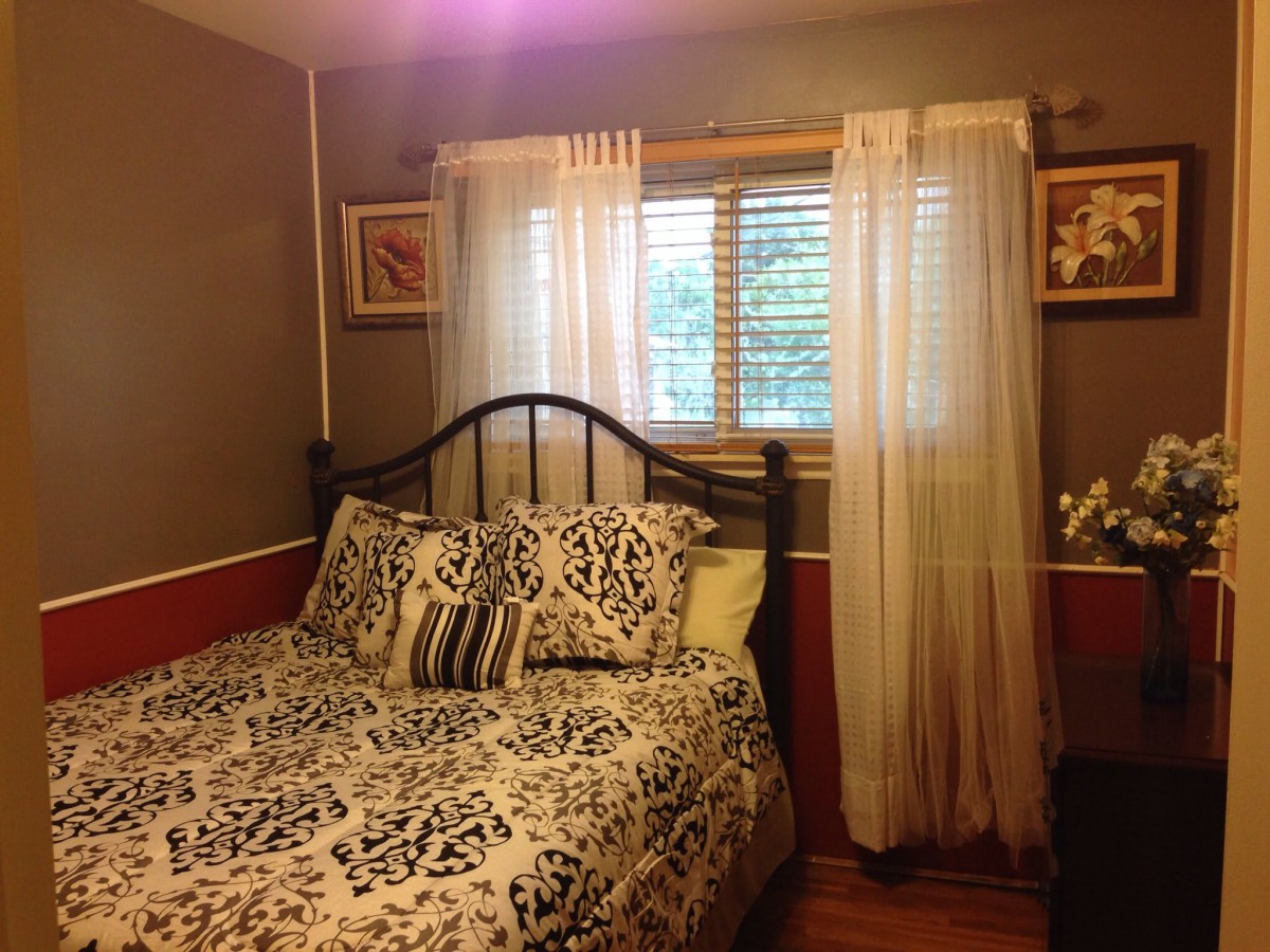 A cozy bedroom with decorative bedding and sheer curtains on the window.