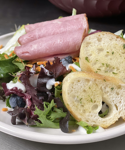 A fresh salad with leafy greens, deli meat, and garlic bread.
