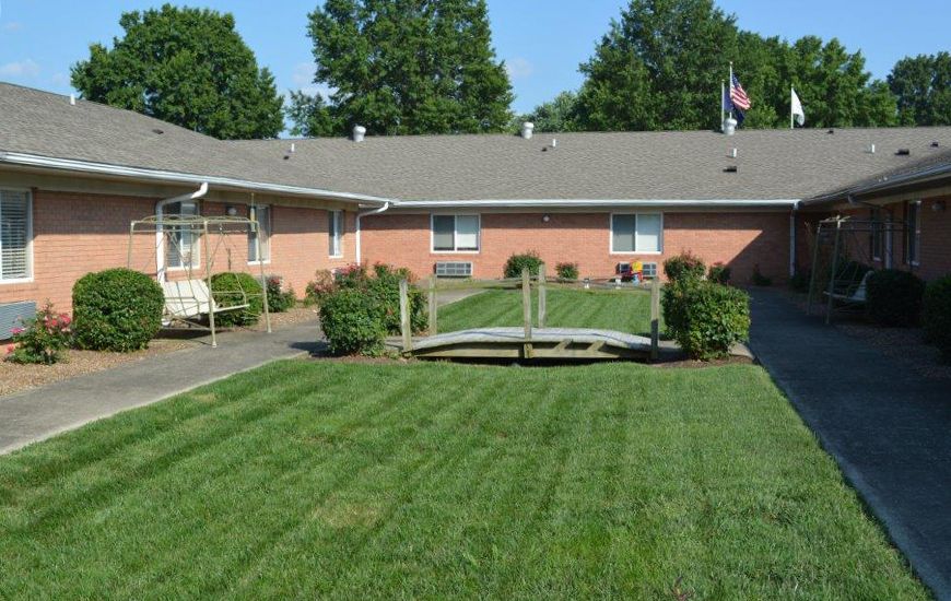 A well-maintained lawn with a small wooden bridge in a garden area, surrounded by a brick building.