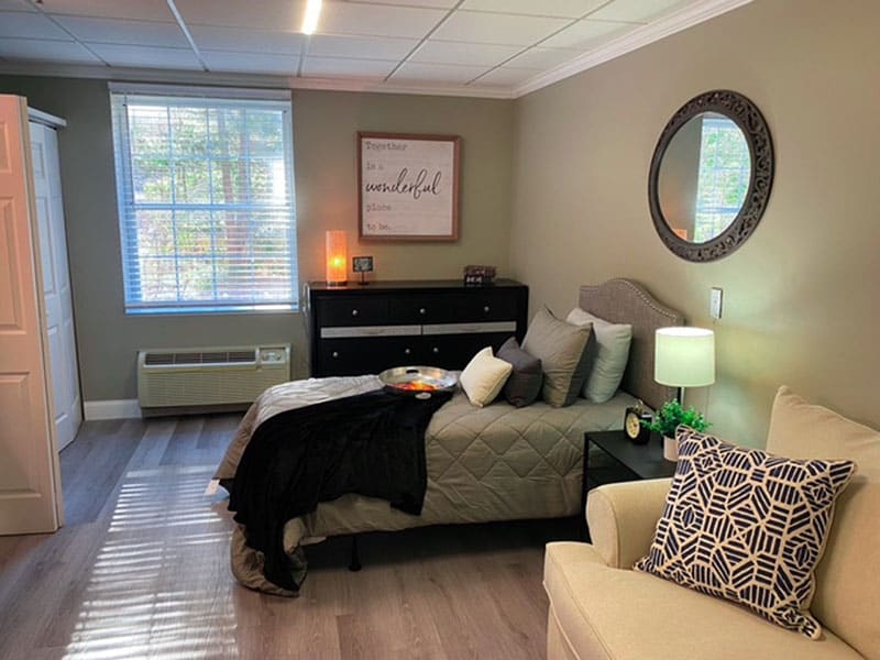 A cozy and well-decorated bedroom featuring a comfortable bed, a mirror on the wall, stylish decor, and soft lighting.