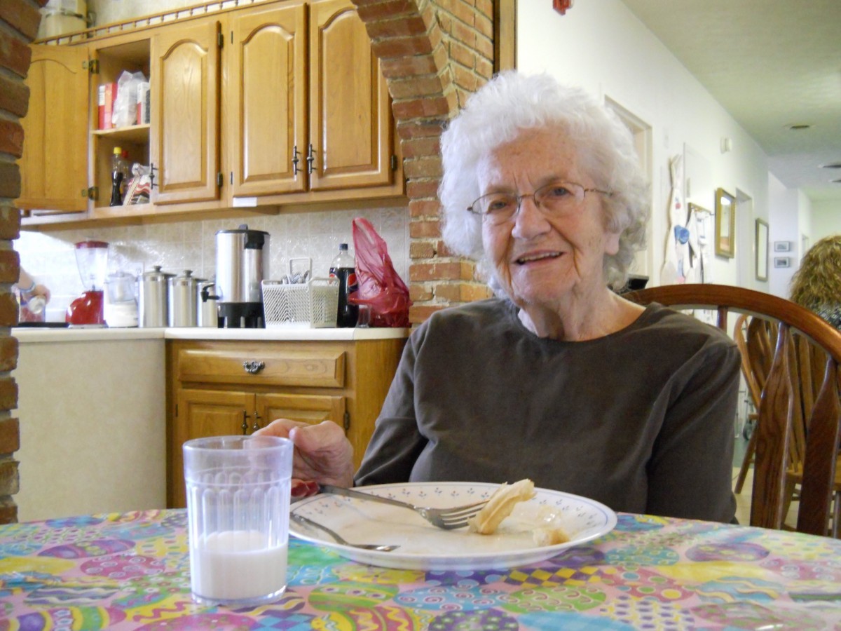 An elderly woman enjoying a meal in her kitchen.