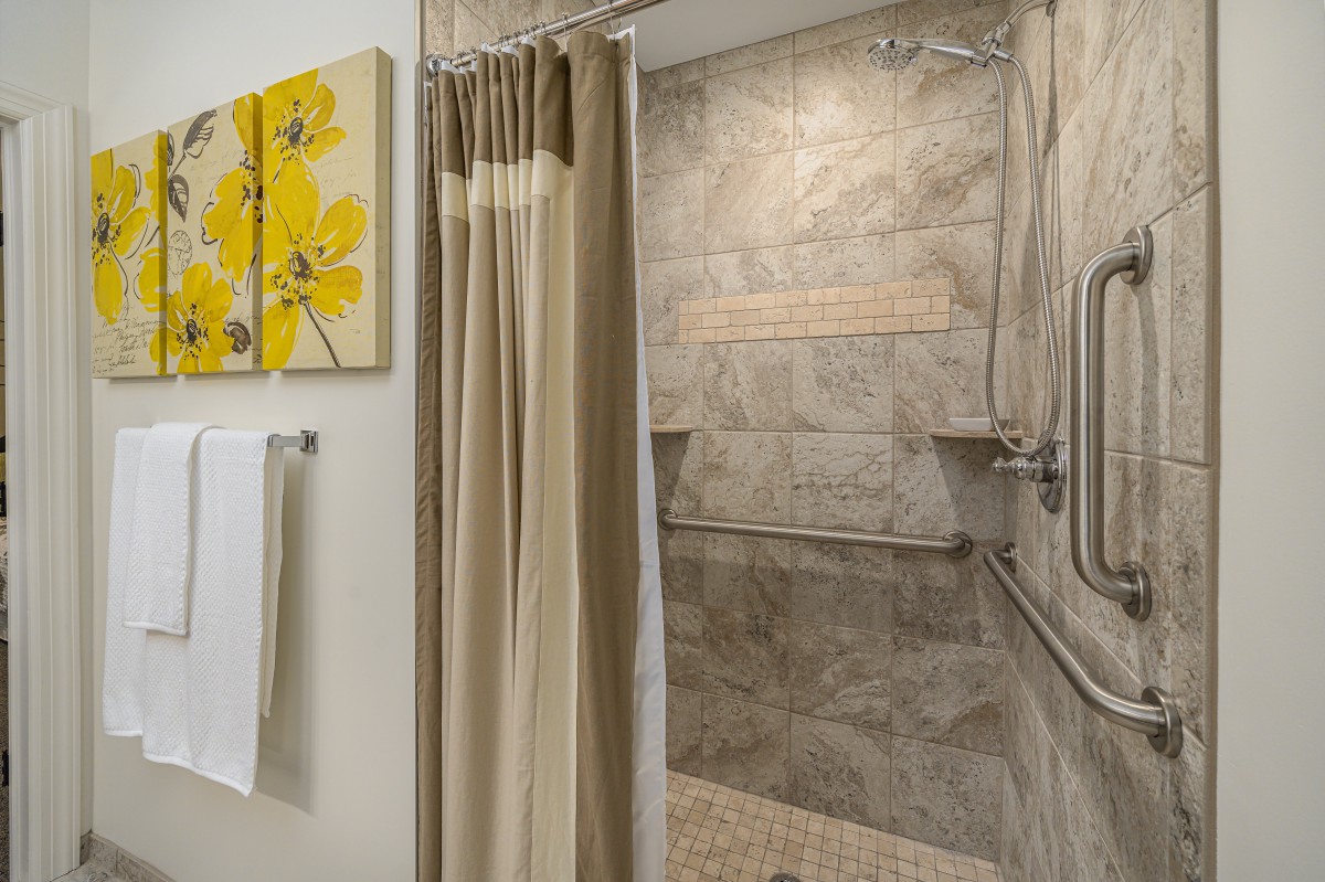 A modern bathroom featuring a tiled shower with grab bars and a neutral-colored shower curtain, complemented by wall art and a towel rack.