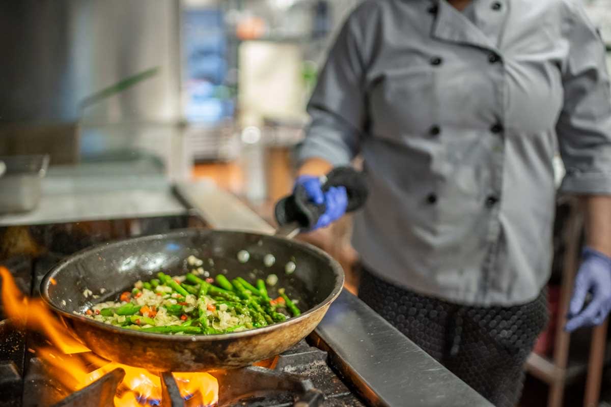 A chef prepares a dish with vegetables in a frying pan on a stove.