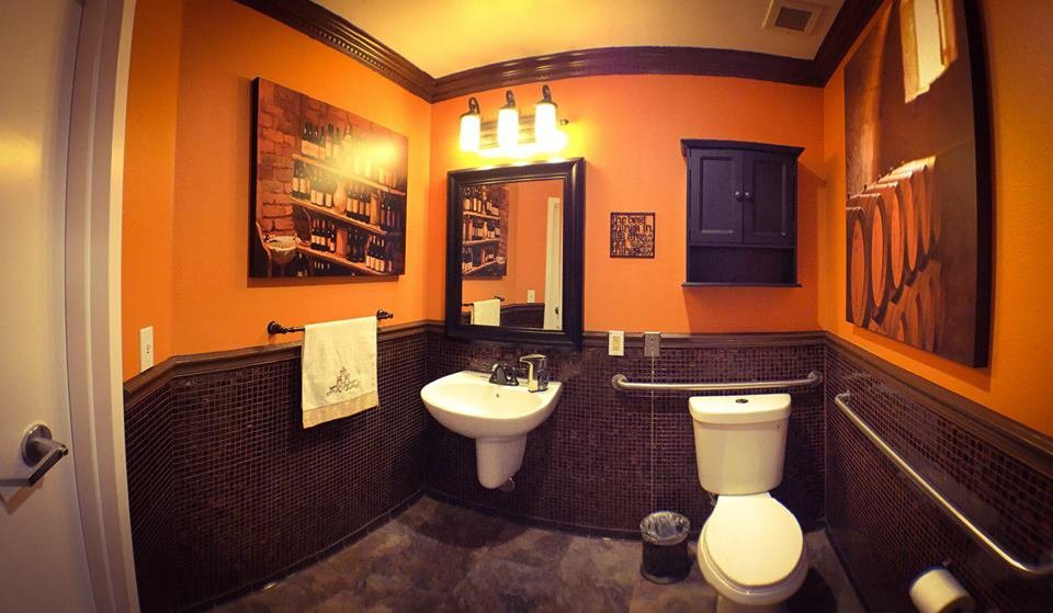 A cozy bathroom with orange walls, featuring a sink, mirror, and toilet.