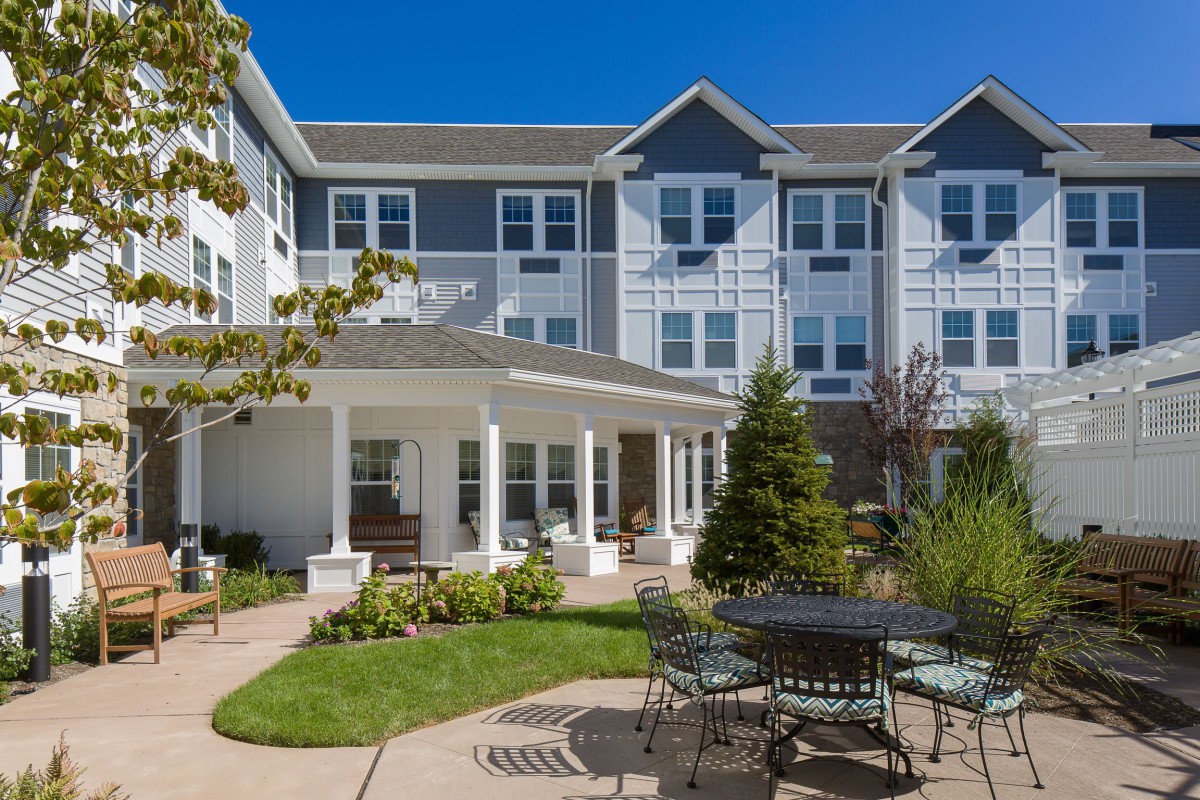 A sunny day view of a residential building with a landscaped garden and outdoor seating area.