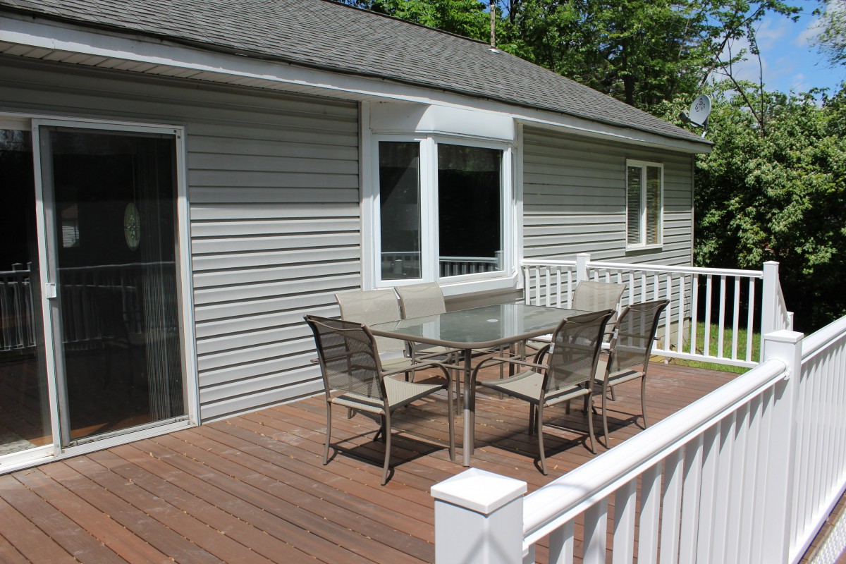 An outdoor deck with a glass patio table and four chairs next to a house.