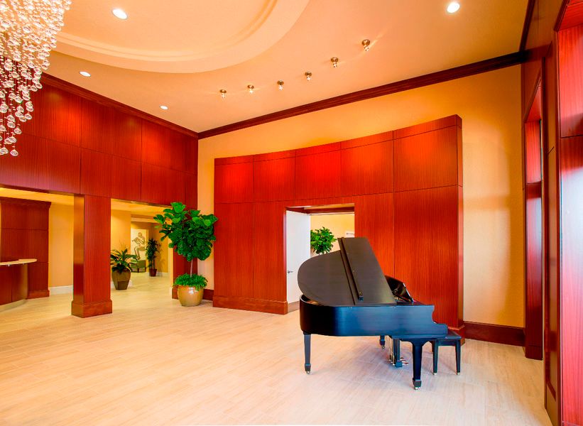 A modern lobby featuring a grand piano, wood paneling, and indoor plants.