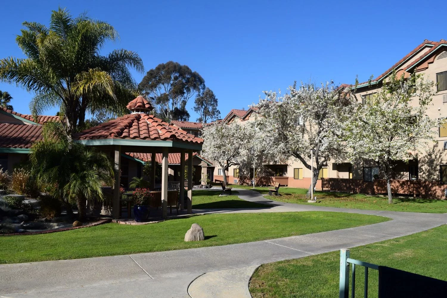 A scenic view of a residential park area with a gazebo, surrounded by trees and a clear blue sky.