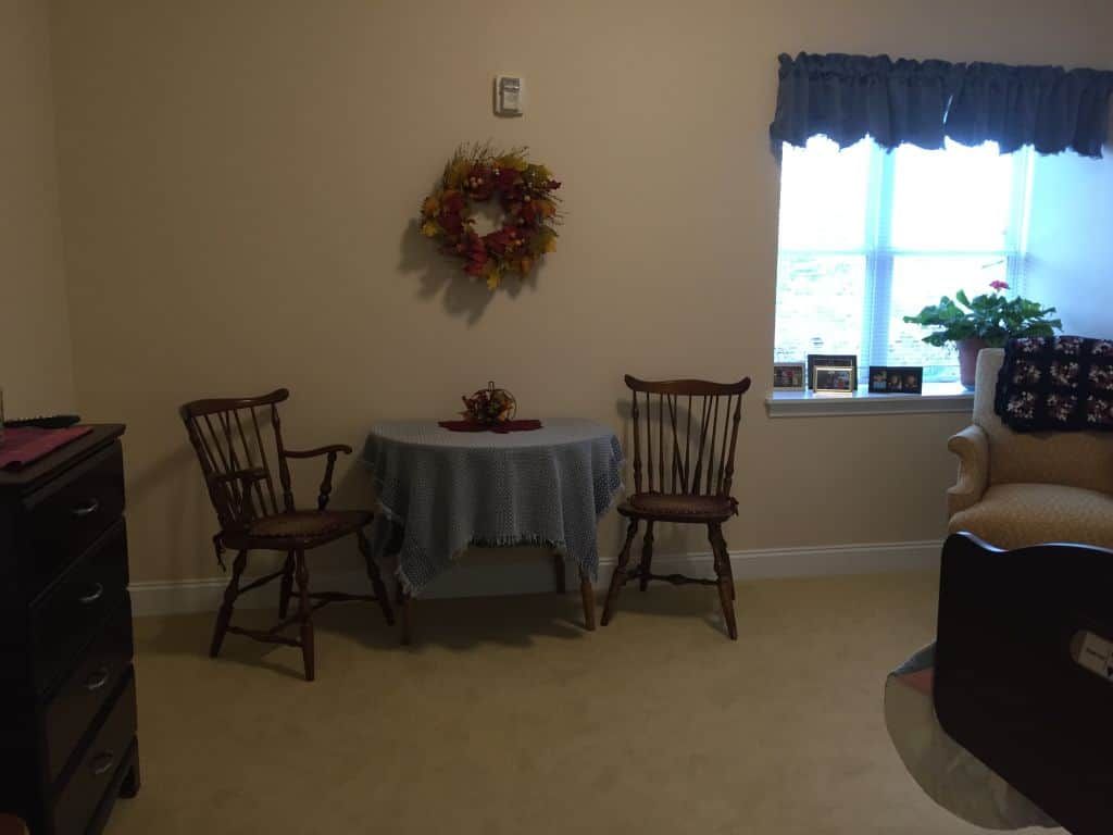 A cozy dining area with a small round table, two wooden chairs, and decorative elements like a wreath on the wall.