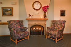 A cozy living room with two floral armchairs flanking a fireplace topped by a clock and vase of flowers.