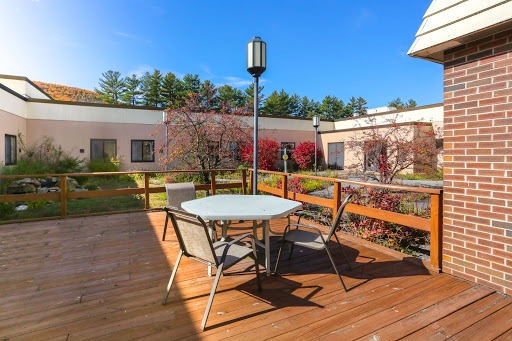 A serene outdoor patio area with a table and chairs, surrounded by blooming trees under a clear blue sky.