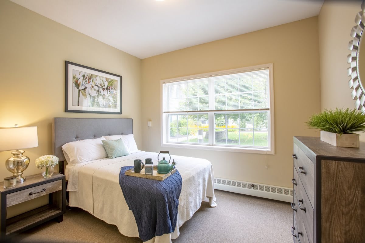 A cozy bedroom with soft lighting, featuring a neatly made bed and a large window overlooking the garden.