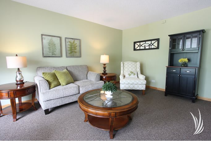 A cozy living room with a sofa, armchair, and wooden coffee table, accented by green walls and decorative artwork.