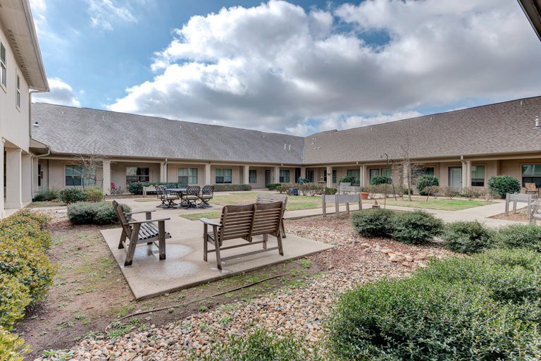 A serene courtyard with outdoor seating and lush landscaping under a partly cloudy sky.