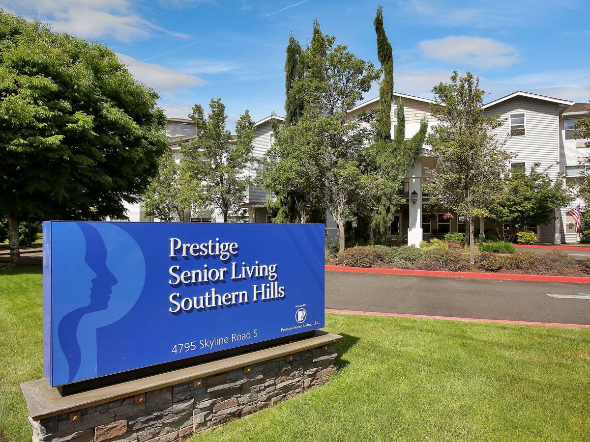 A senior living facility with a landscaped exterior and prominent signage under a clear blue sky.