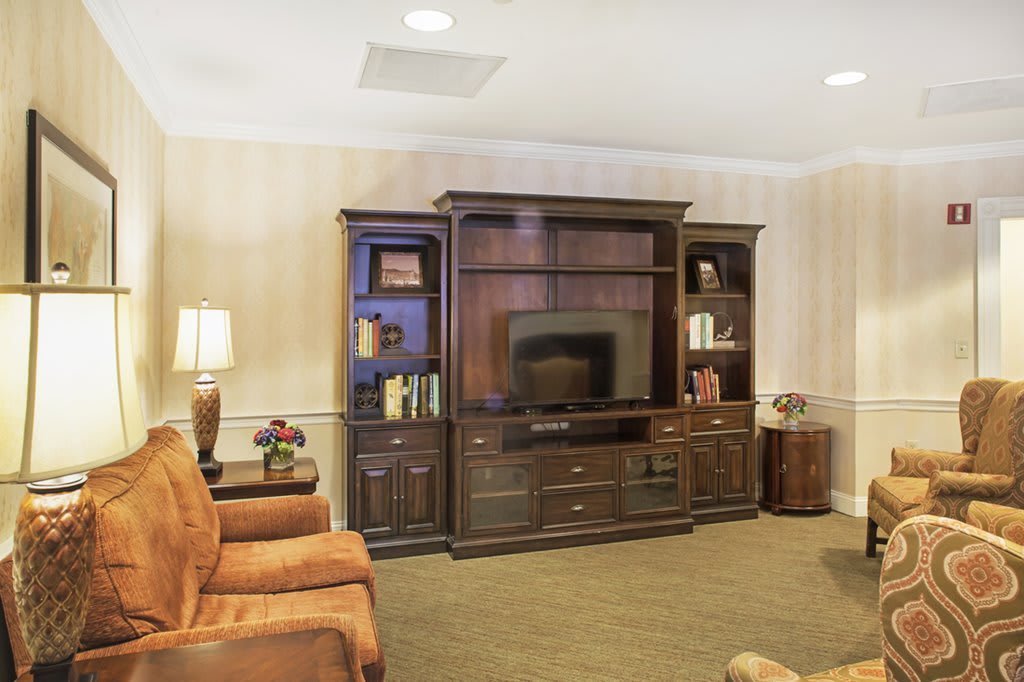 A cozy living room with a large entertainment center featuring a television and shelves, surrounded by comfortable armchairs and warm lighting.
