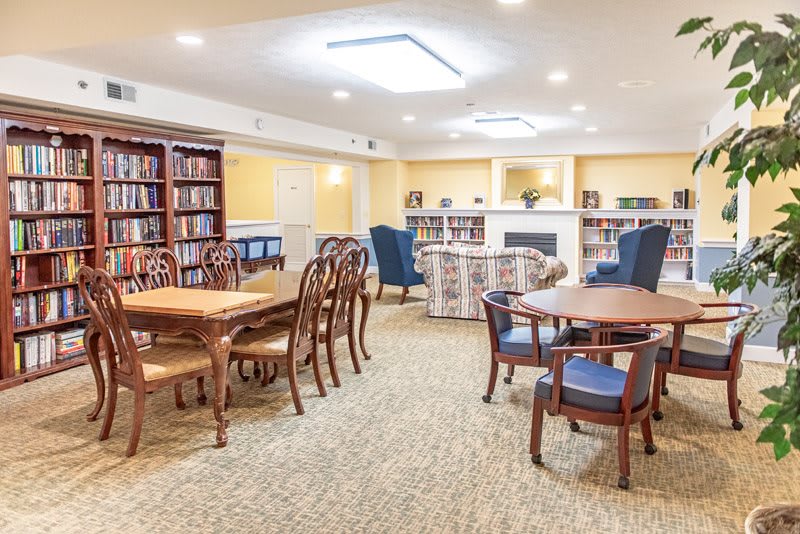 A cozy library interior with wooden tables and chairs, surrounded by bookshelves.