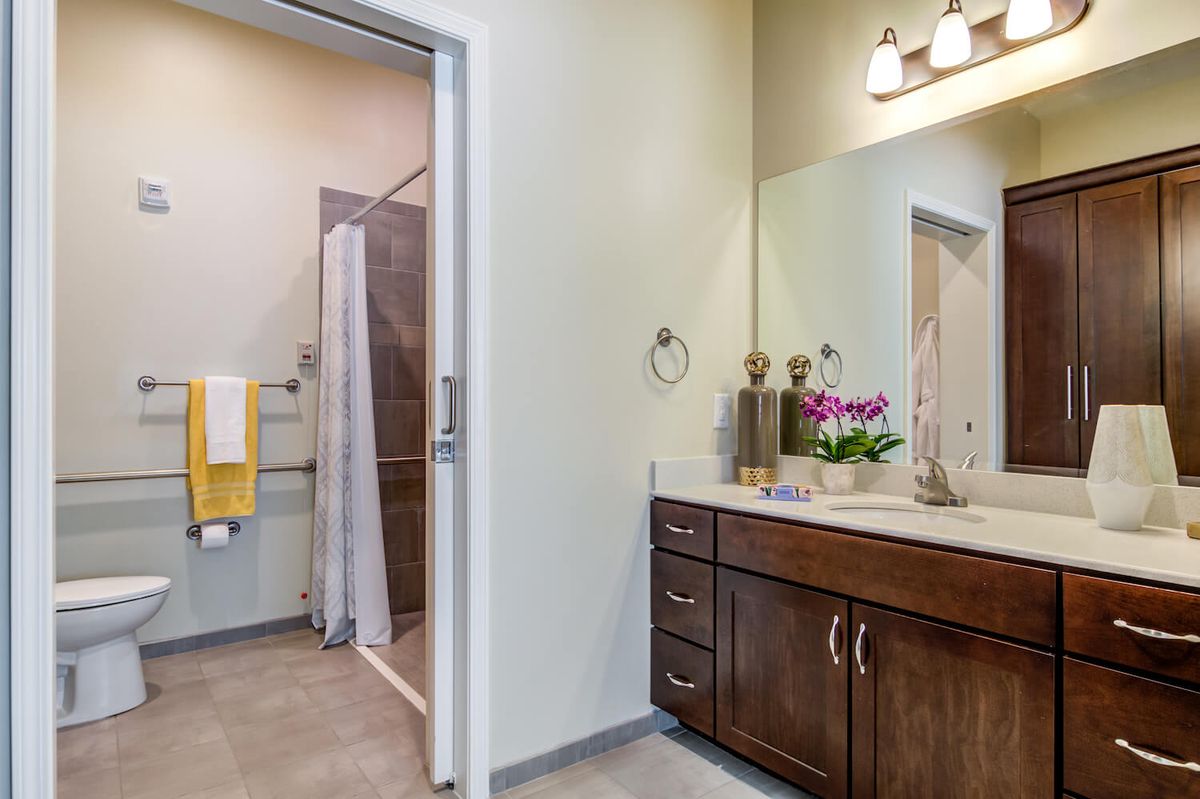 A modern bathroom with a wooden cabinet, large mirror, and shower area.