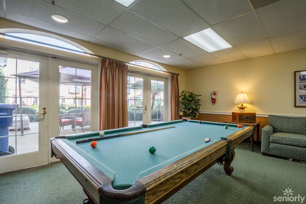 A cozy game room featuring a billiards table with natural light streaming through large windows.