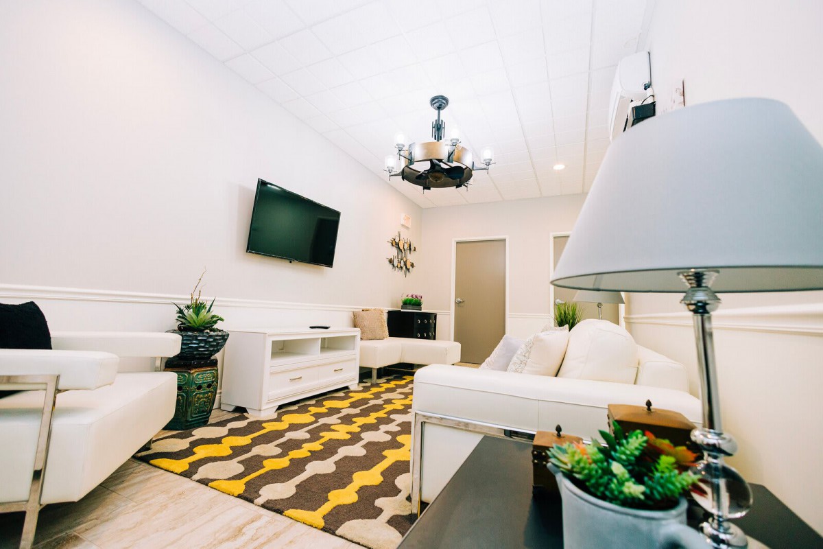 A modern living room with white furniture, a geometric rug, and decorative plants.