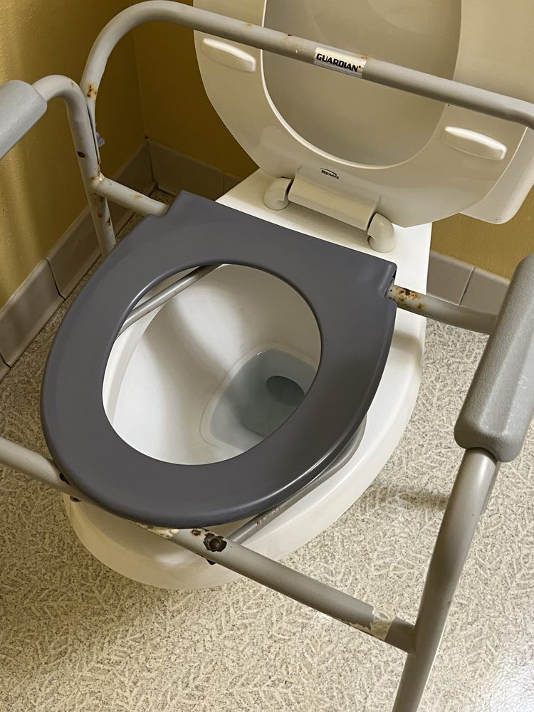 A toilet with an elevated seat and handrails for accessibility.