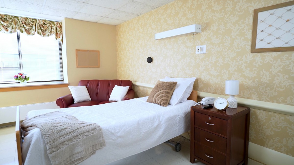 A hospital room with a neatly made bed and a couch in the corner.