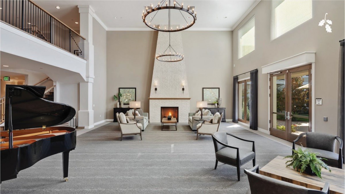 A spacious living room with modern decor, featuring a fireplace and high ceilings adorned with elegant chandeliers.