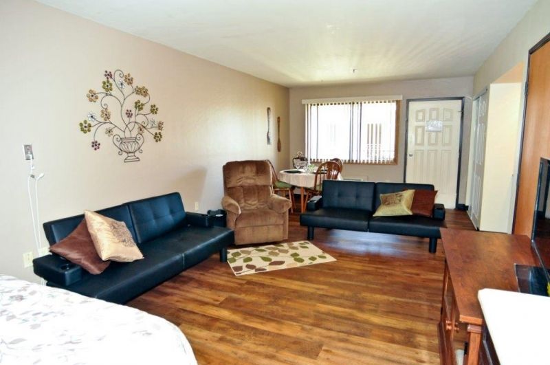A cozy living room with modern furnishings, featuring two black sofas, a recliner, and hardwood flooring.