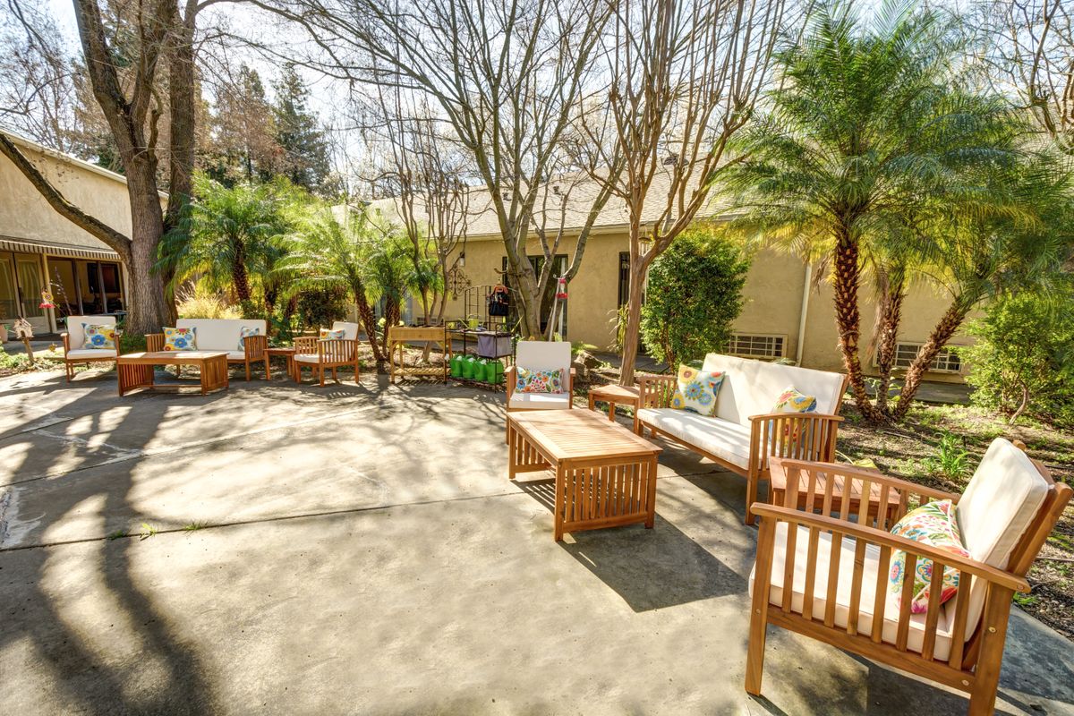 A sunny outdoor patio area with wooden furniture surrounded by trees.