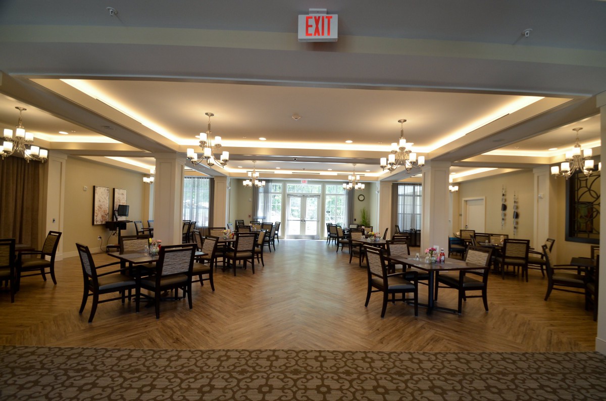 A spacious and elegant dining area with multiple tables and chairs arranged symmetrically under warm lighting.