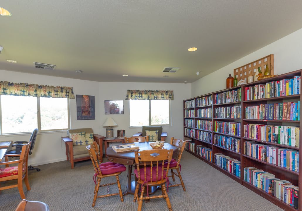 A cozy library room with bookshelves, a table with chairs, and windows letting in natural light.