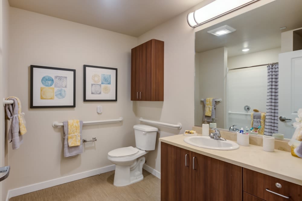 A modern bathroom with wooden cabinets, artwork on the walls, and neatly arranged towels.