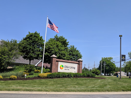 Entrance sign for a community or facility with an American flag and landscaped surroundings.
