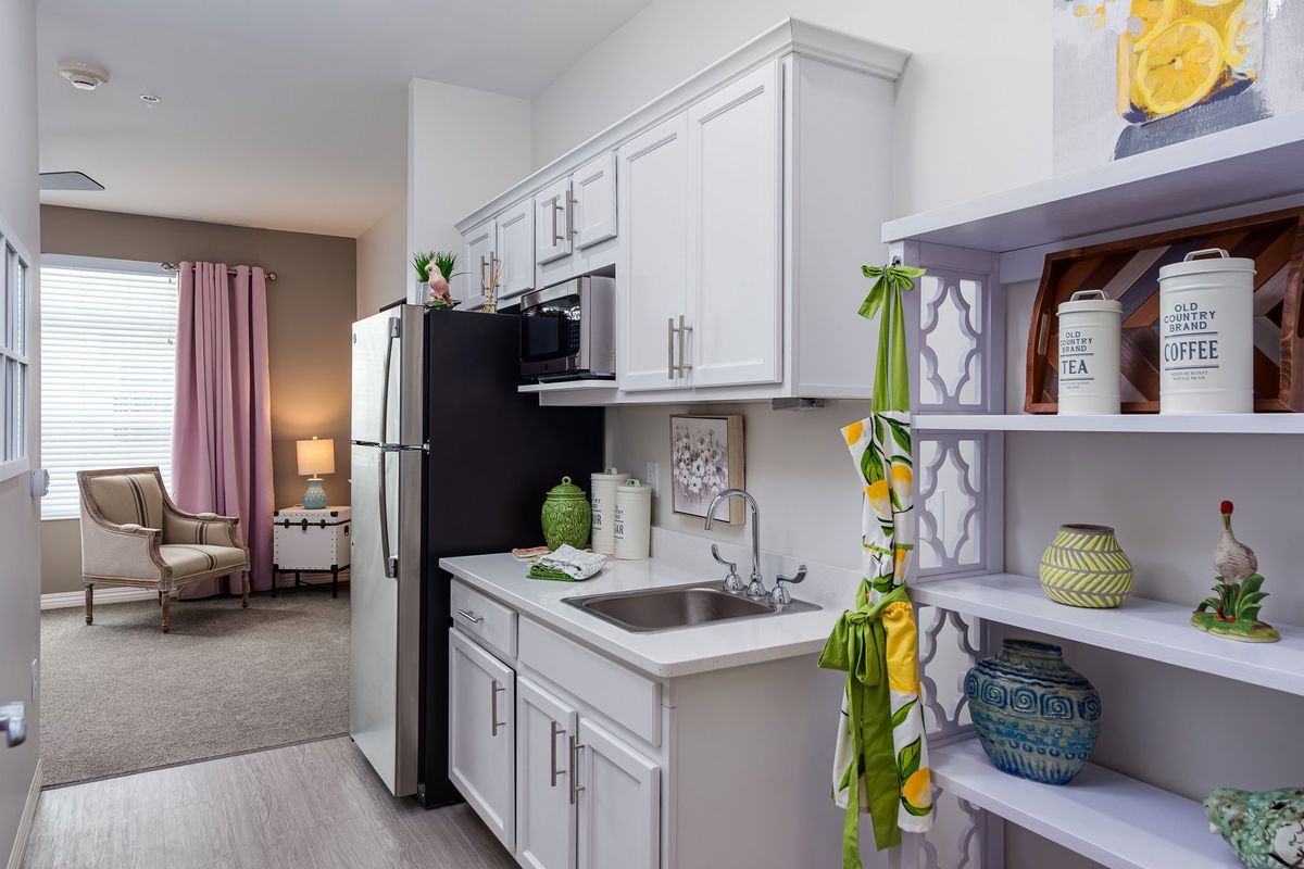 A modern apartment kitchen with white cabinets and a black refrigerator.