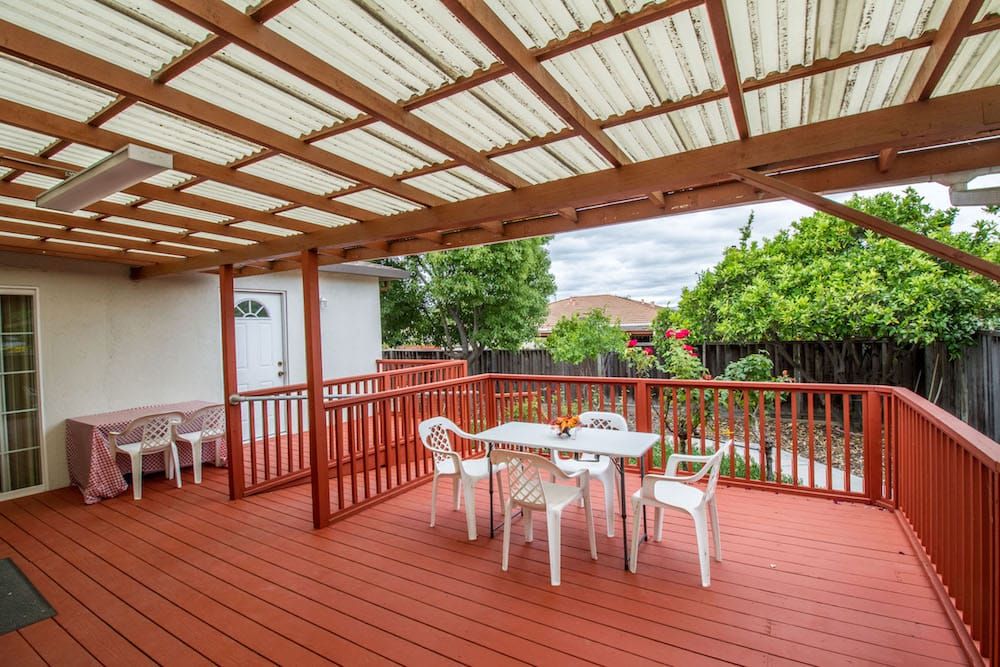 A spacious wooden deck with a pergola, featuring outdoor seating and surrounded by greenery.
