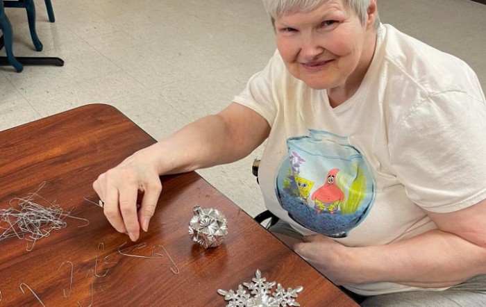 A woman sitting at a table and working on crafting decorations, smiling warmly.