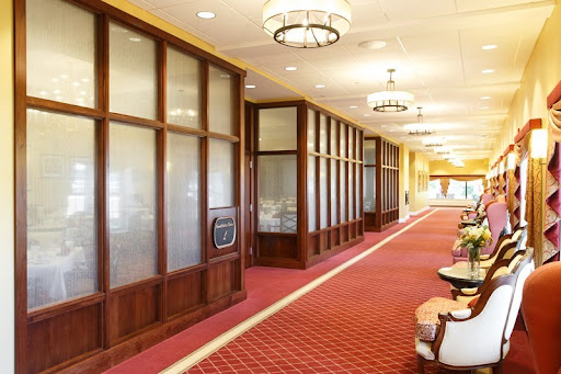 A well-lit hotel hallway featuring elegant wooden panels and a plush carpet.