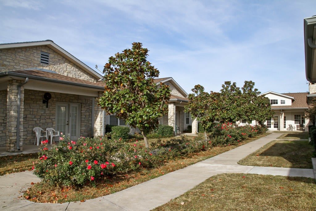 A building with a landscaped walkway lined with trees and shrubs on a clear day.